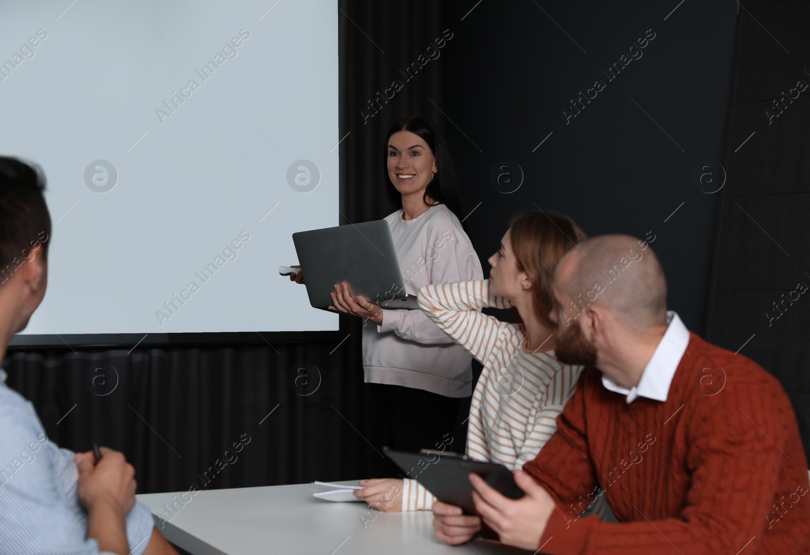 Photo of Business people listening to speaker in conference room with video projection screen