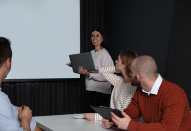 Photo of Business people listening to speaker in conference room with video projection screen