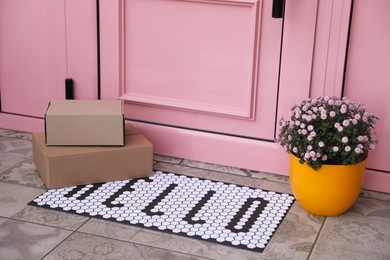 Photo of Cardboard boxes on stylish door mat and beautiful flowers near entrance