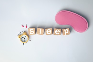 Photo of Word Sleep made of wooden cubes near blindfold, pills and alarm clock on white background, flat lay. Insomnia treatment
