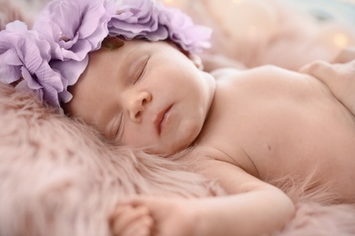 Adorable newborn baby girl with floral headband sleeping on bed