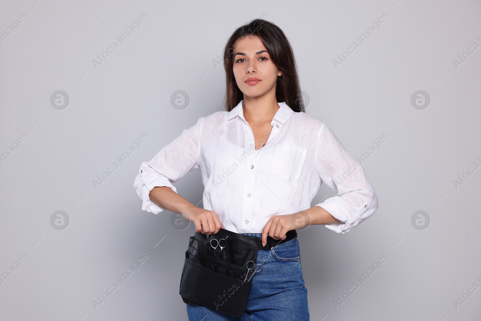 Photo of Portrait of happy hairdresser with professional tools on light grey background