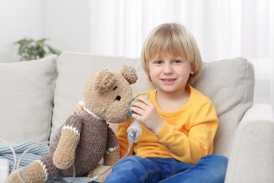 Photo of Happy boy with toy bear and nebulizer for inhalation at home