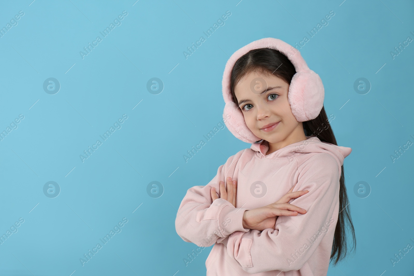 Photo of Cute little girl wearing stylish earmuffs on light blue background. Space for text