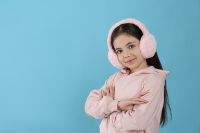 Photo of Cute little girl wearing stylish earmuffs on light blue background. Space for text