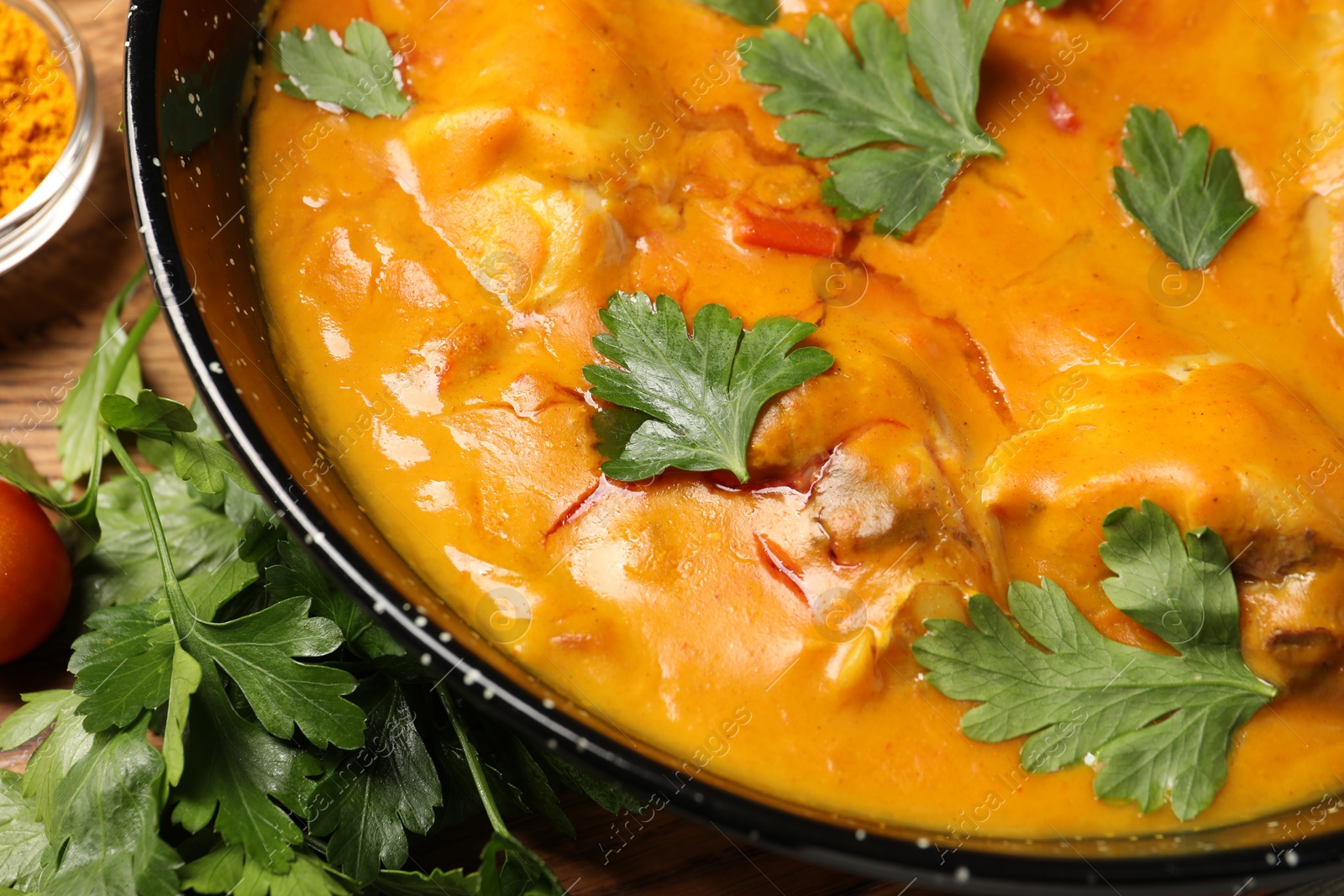 Photo of Tasty chicken curry with parsley and ingredients on wooden table, flat lay