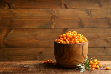 Photo of Fresh ripe sea buckthorn in bowl on wooden table. Space for text