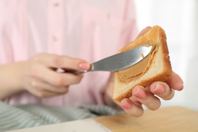 Photo of Woman spreading tasty nut butter onto toast at table, closeup