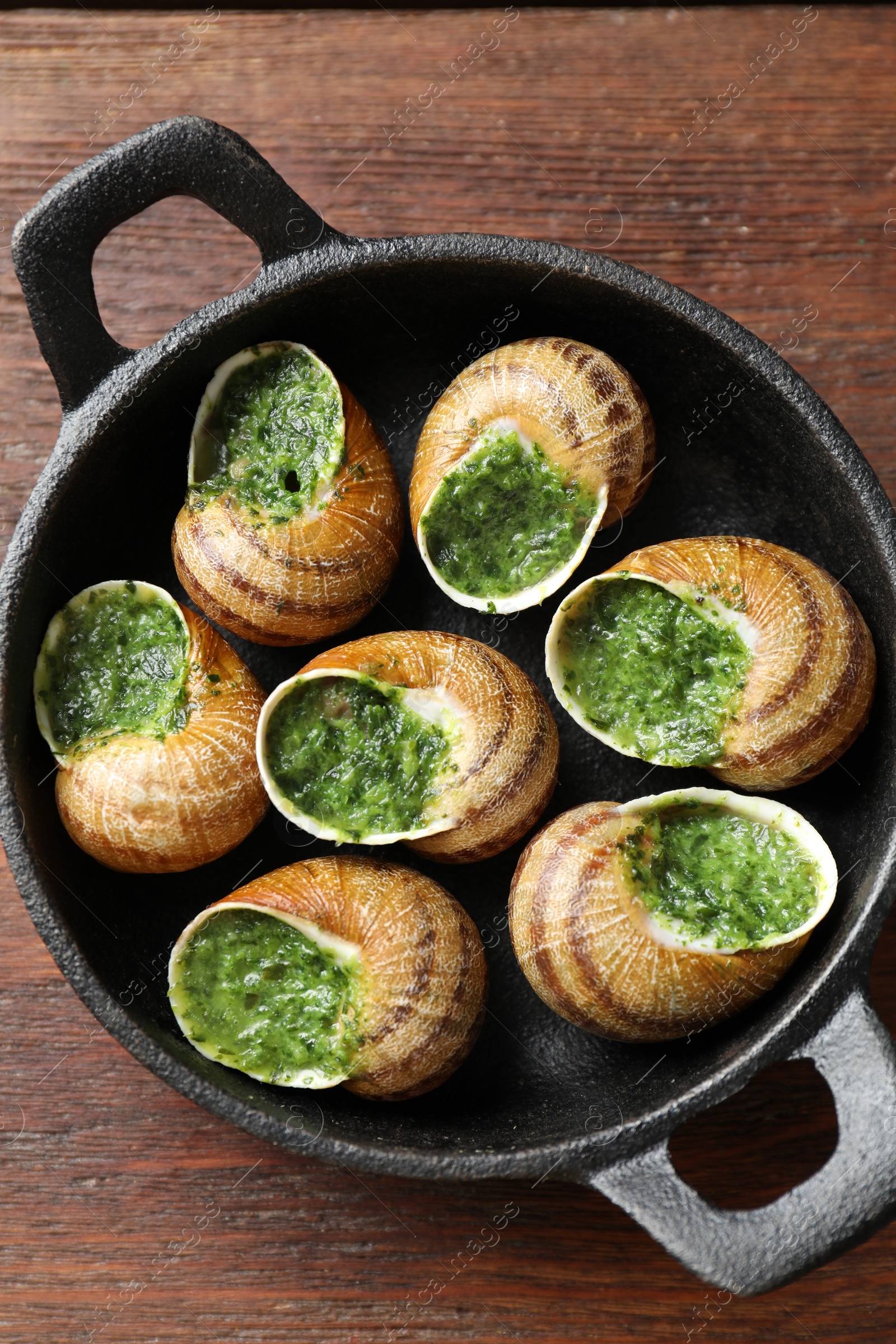 Photo of Delicious cooked snails in baking dish on wooden table, top view