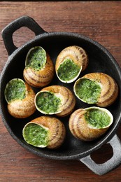 Delicious cooked snails in baking dish on wooden table, top view