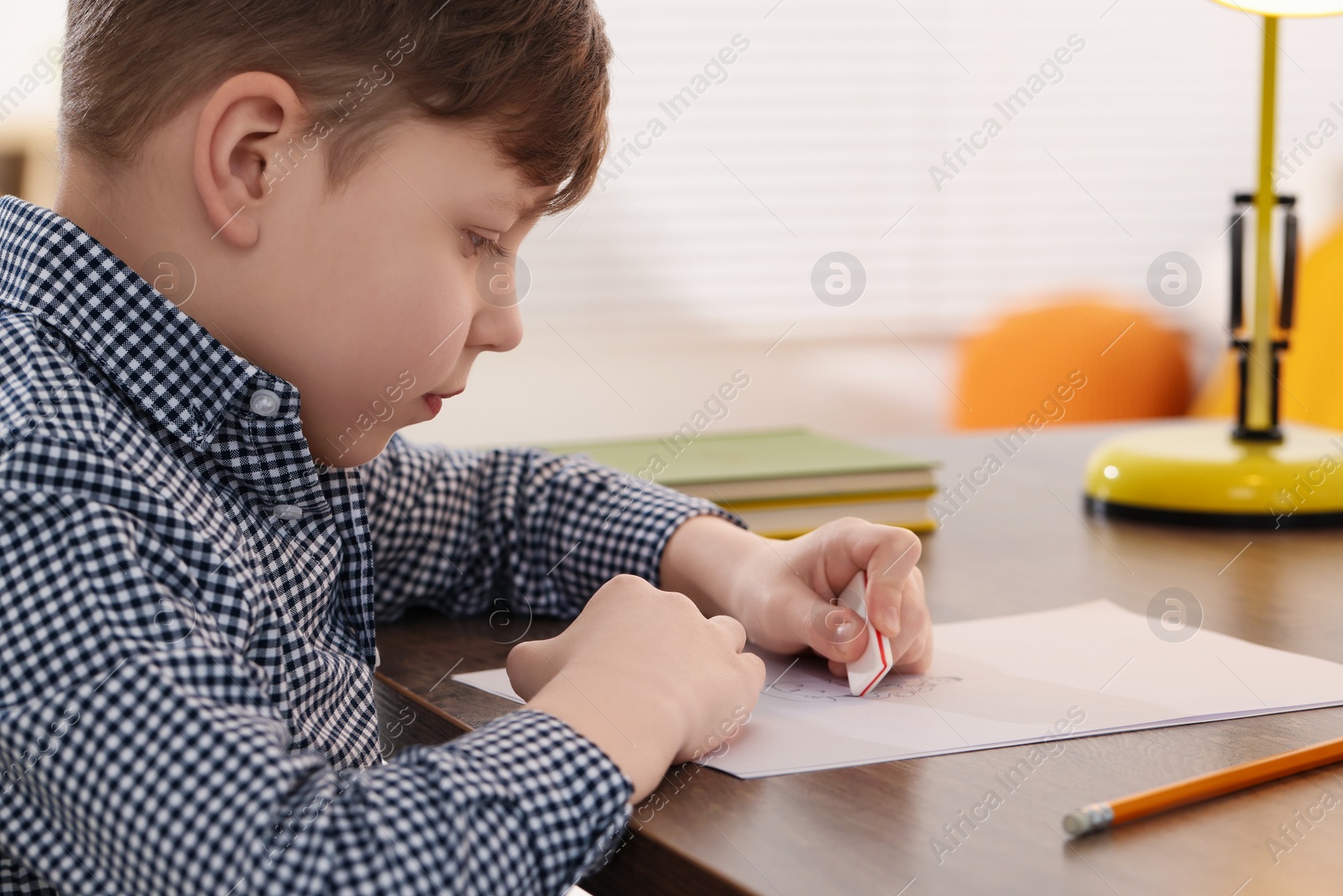 Photo of Little boy erasing mistake in his notebook at wooden desk indoors