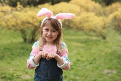 Photo of Easter celebration. Cute little girl with bunny ears outdoors, space for text