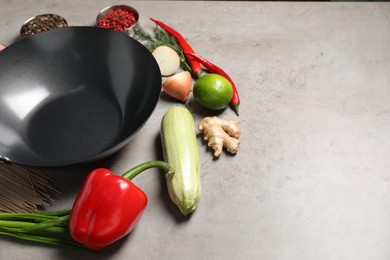 Empty iron wok and raw ingredients on grey table. Space for text