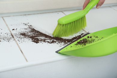 Woman sweeping away scattered soil from window sill with brush, closeup