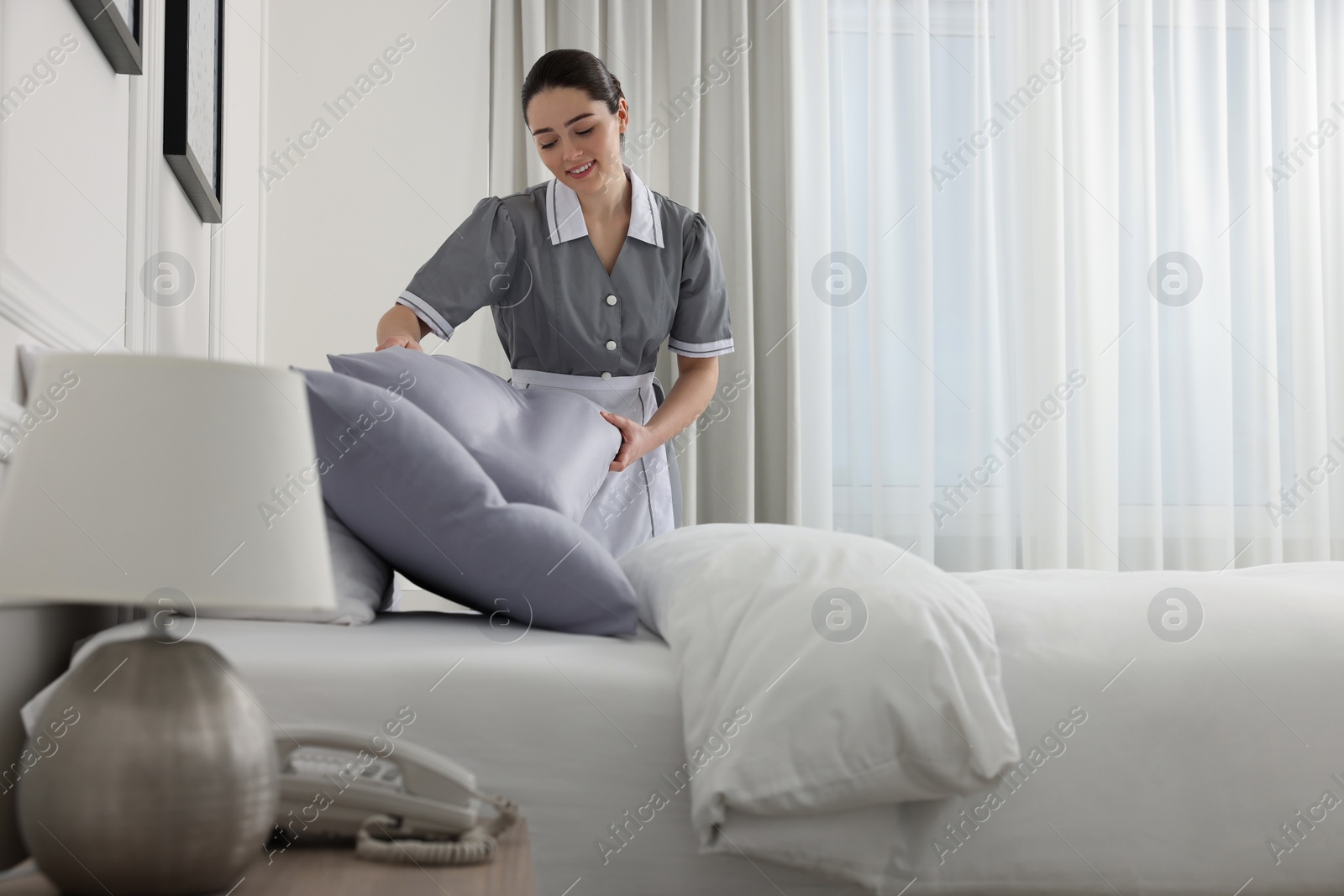 Photo of Young maid making bed in hotel room