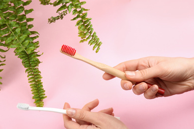 Photo of Woman holding natural bamboo and plastic toothbrushes on pink background