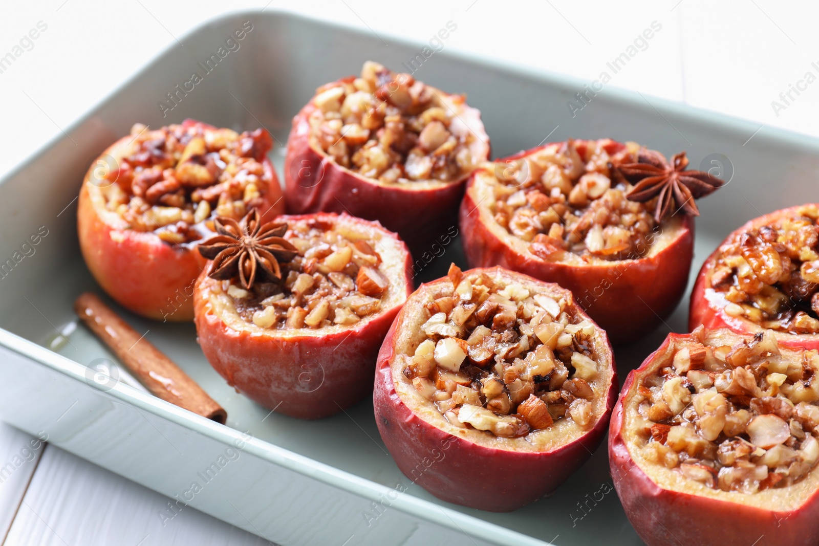 Photo of Tasty baked apples with nuts, honey and spices in dish on white table, closeup