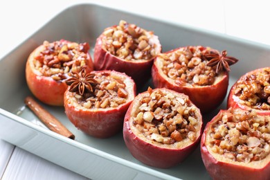 Photo of Tasty baked apples with nuts, honey and spices in dish on white table, closeup