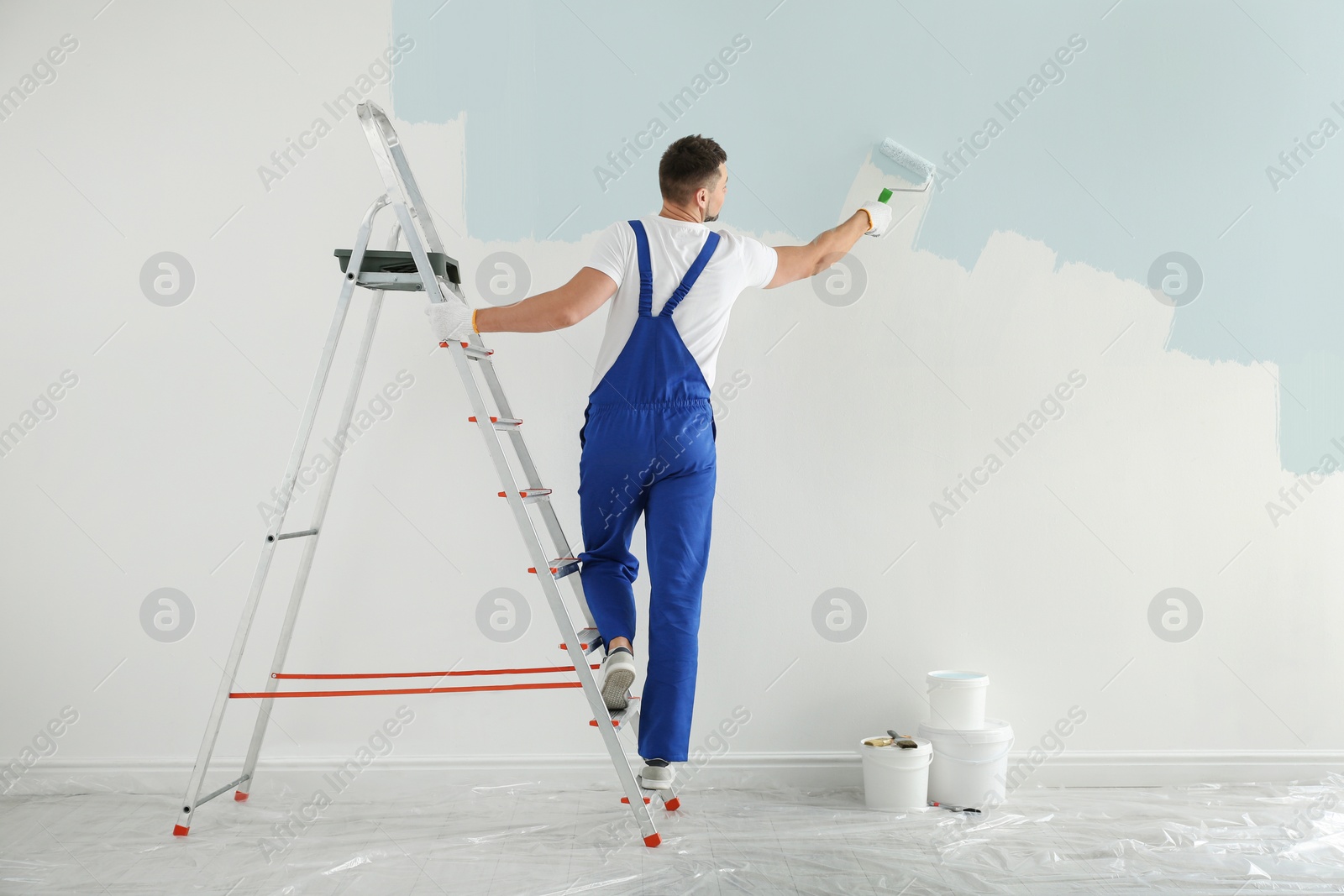 Image of Man painting wall with light blue dye indoors, back view