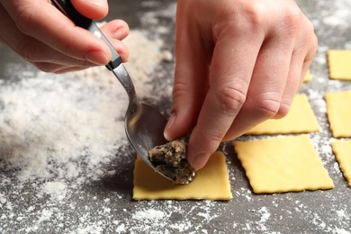 Woman making ravioli at grey table, closeup. Italian pasta