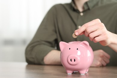 Photo of Financial savings. Man putting coin into piggy bank at wooden table, closeup