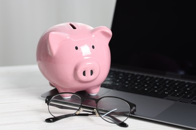 Photo of Piggy bank, glasses and laptop on white table