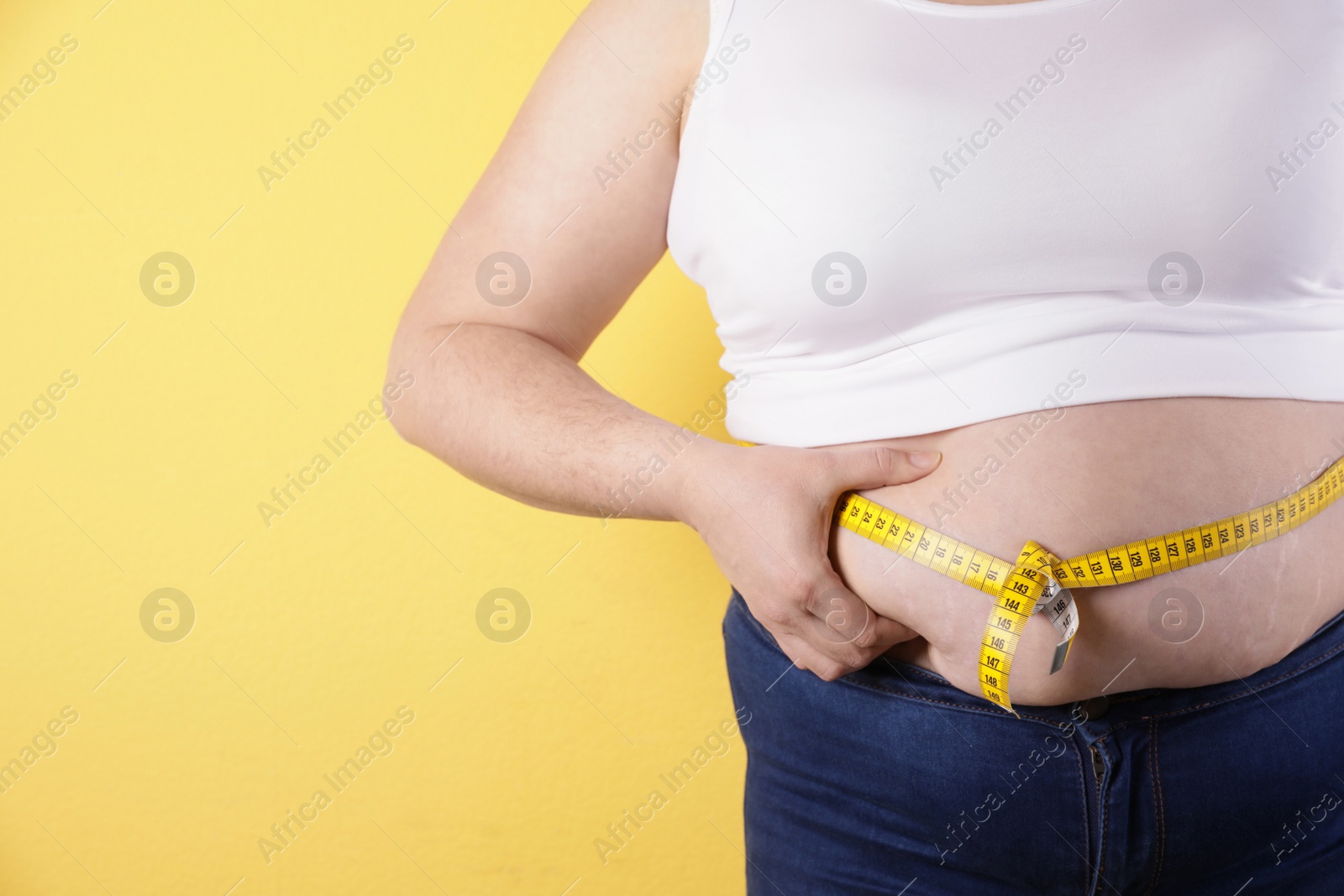 Photo of Overweight woman measuring waist with tape on color background, closeup. Space for text
