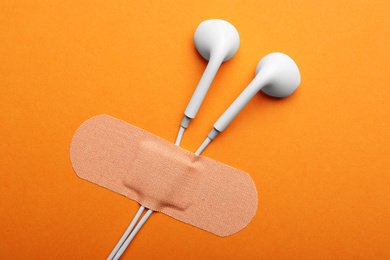 Photo of Wired earphones with sticking plaster on orange background, flat lay