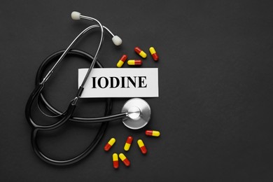Photo of Card with word Iodine, stethoscope and pills on black background, flat lay. Space for text