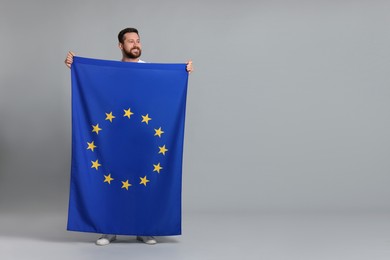 Man holding European Union flag on light grey background, space for text