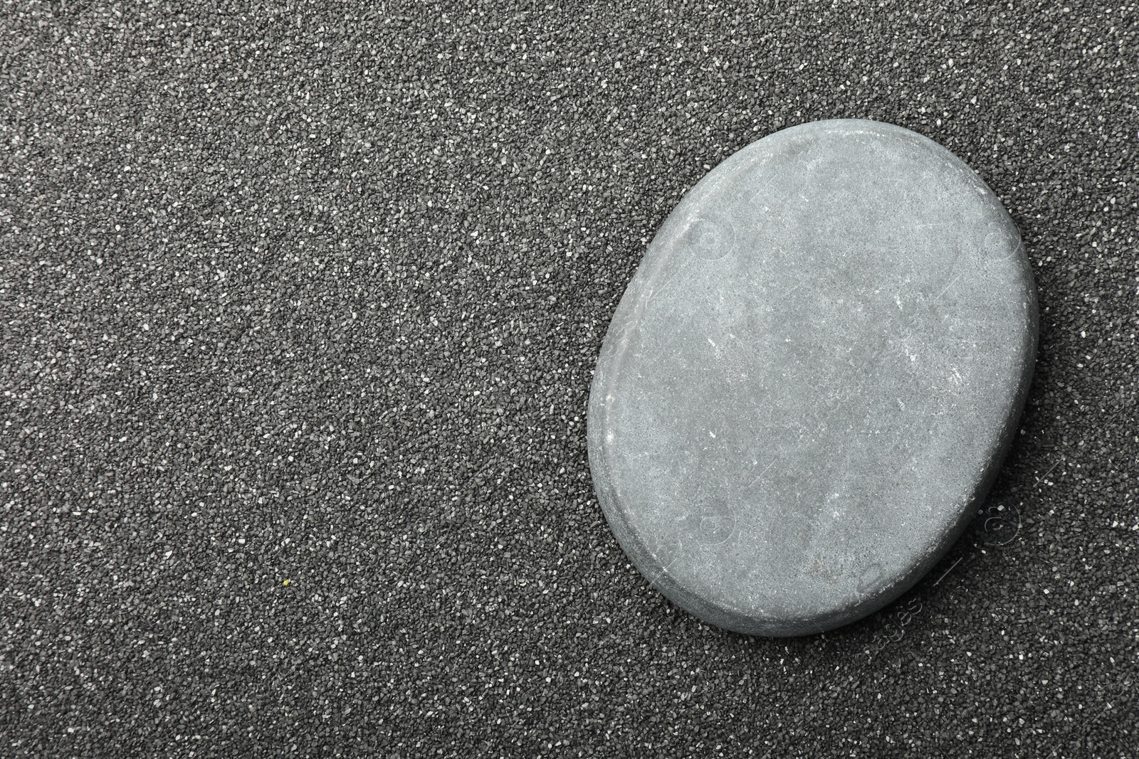 Photo of Presentation of product. Stone podium on black sand, top view. Space for text