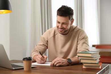 Photo of Man with laptop and books studying at table in library