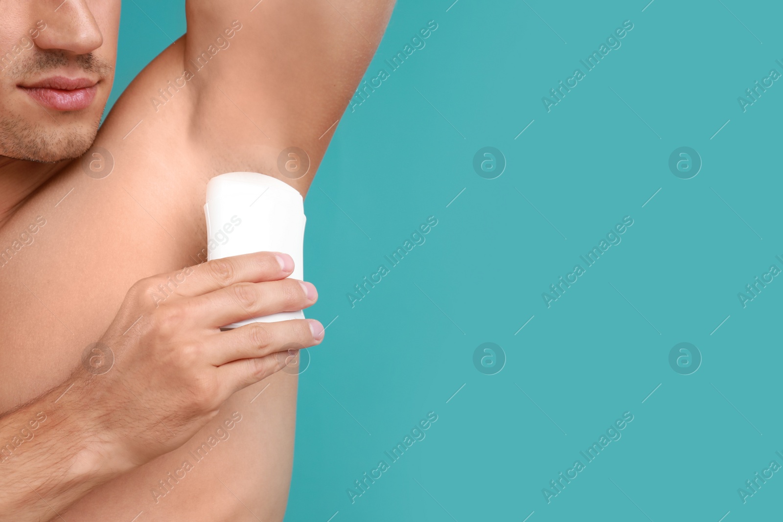 Photo of Young man applying deodorant to armpit on light blue background, closeup. Space for text