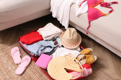 Open suitcase with different women clothes and accessories on carpet