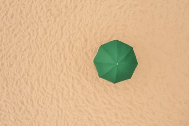 Image of Green beach umbrella on sandy coast, aerial view. Space for text