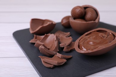 Broken and whole chocolate eggs with paste on white wooden table, closeup