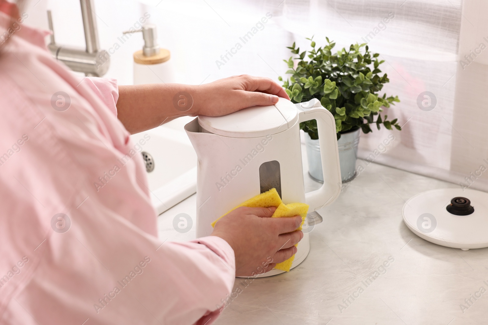 Photo of Woman cleaning electric kettle with sponge at countertop in kitchen, closeup