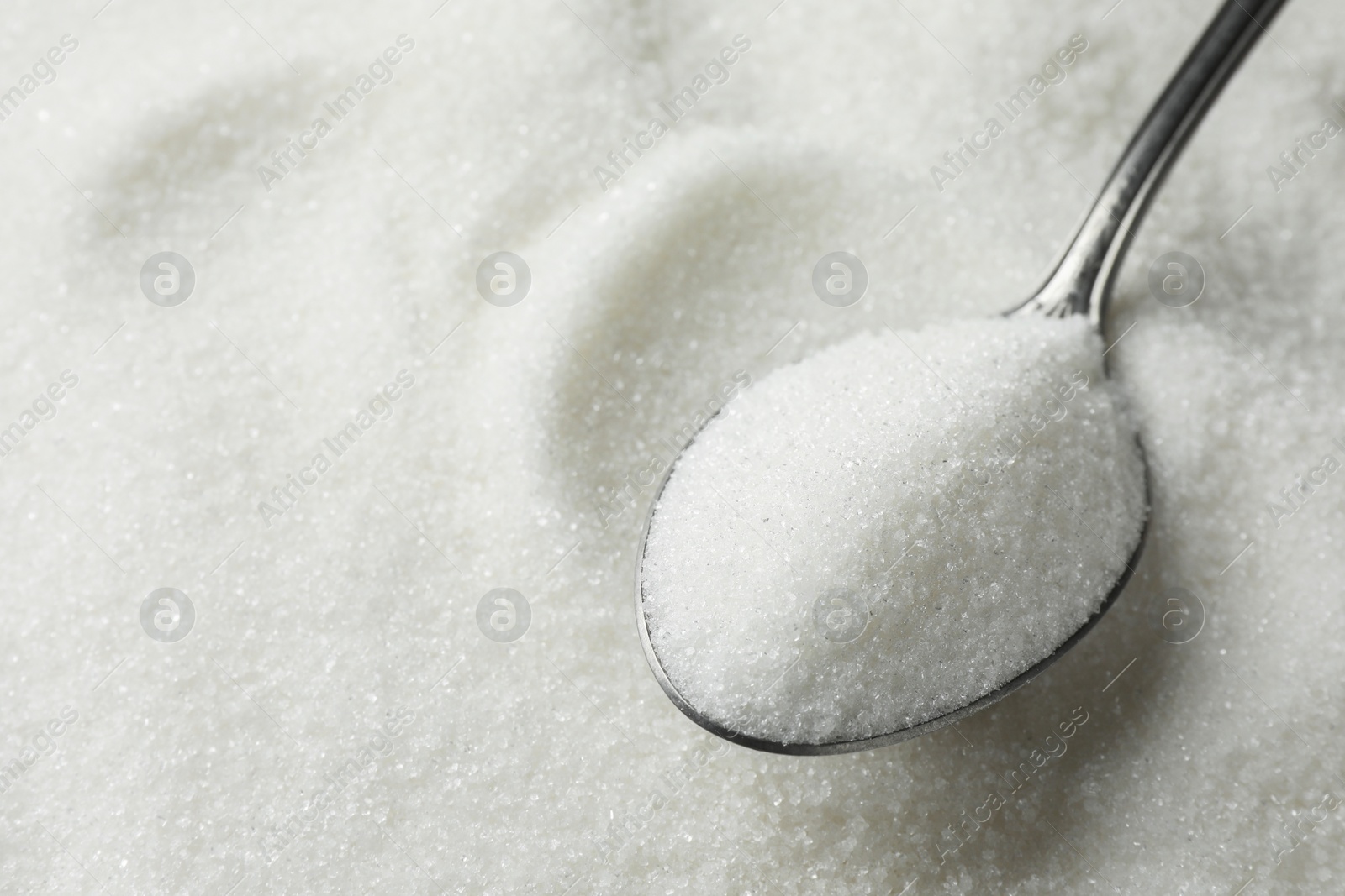 Photo of Metal spoon on granulated sugar, closeup view