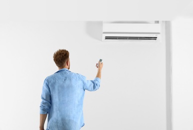Photo of Young man operating air conditioner with remote control indoors. Space for text