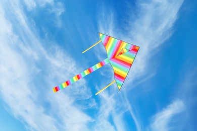 Image of Bright striped rainbow kite flying in blue sky on sunny day