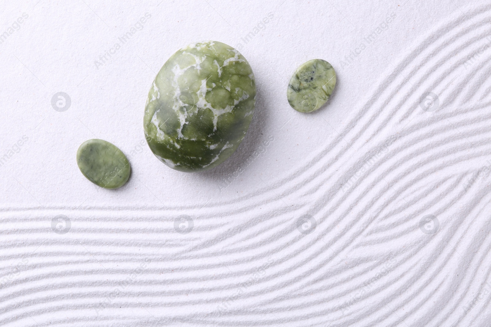 Photo of Zen garden stones on white sand with pattern, flat lay