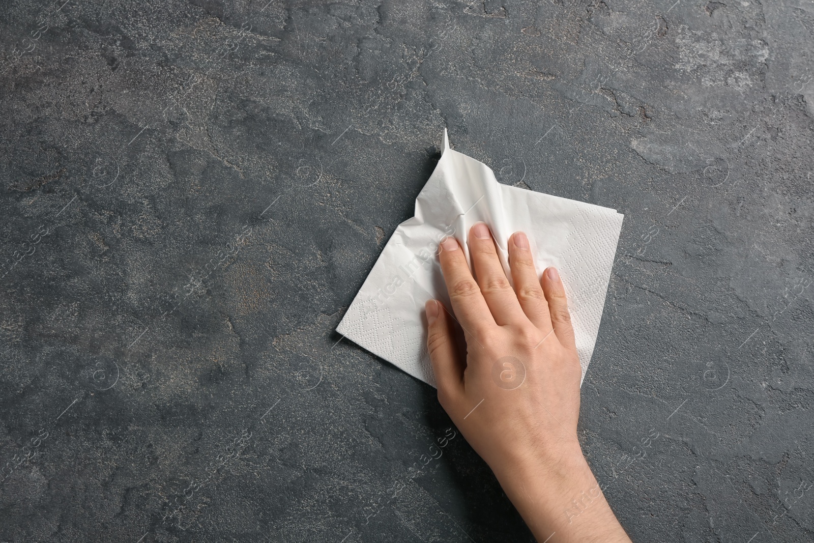 Photo of Woman wiping grey table with paper napkin, top view. Space for text