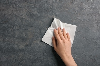 Photo of Woman wiping grey table with paper napkin, top view. Space for text