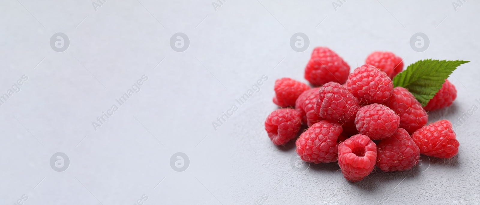 Photo of Delicious fresh ripe raspberries with green leaf on light grey table