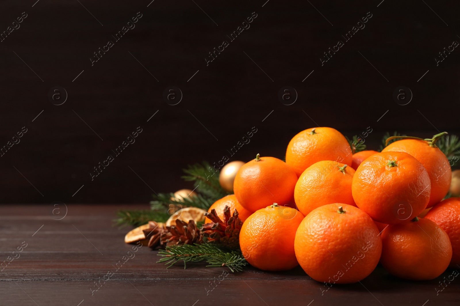 Photo of Fresh tangerines with fir tree branches on dark wooden table, space for text. Christmas atmosphere