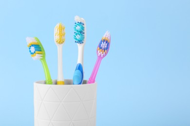 Photo of Different toothbrushes in holder on light blue background, closeup. Space for text