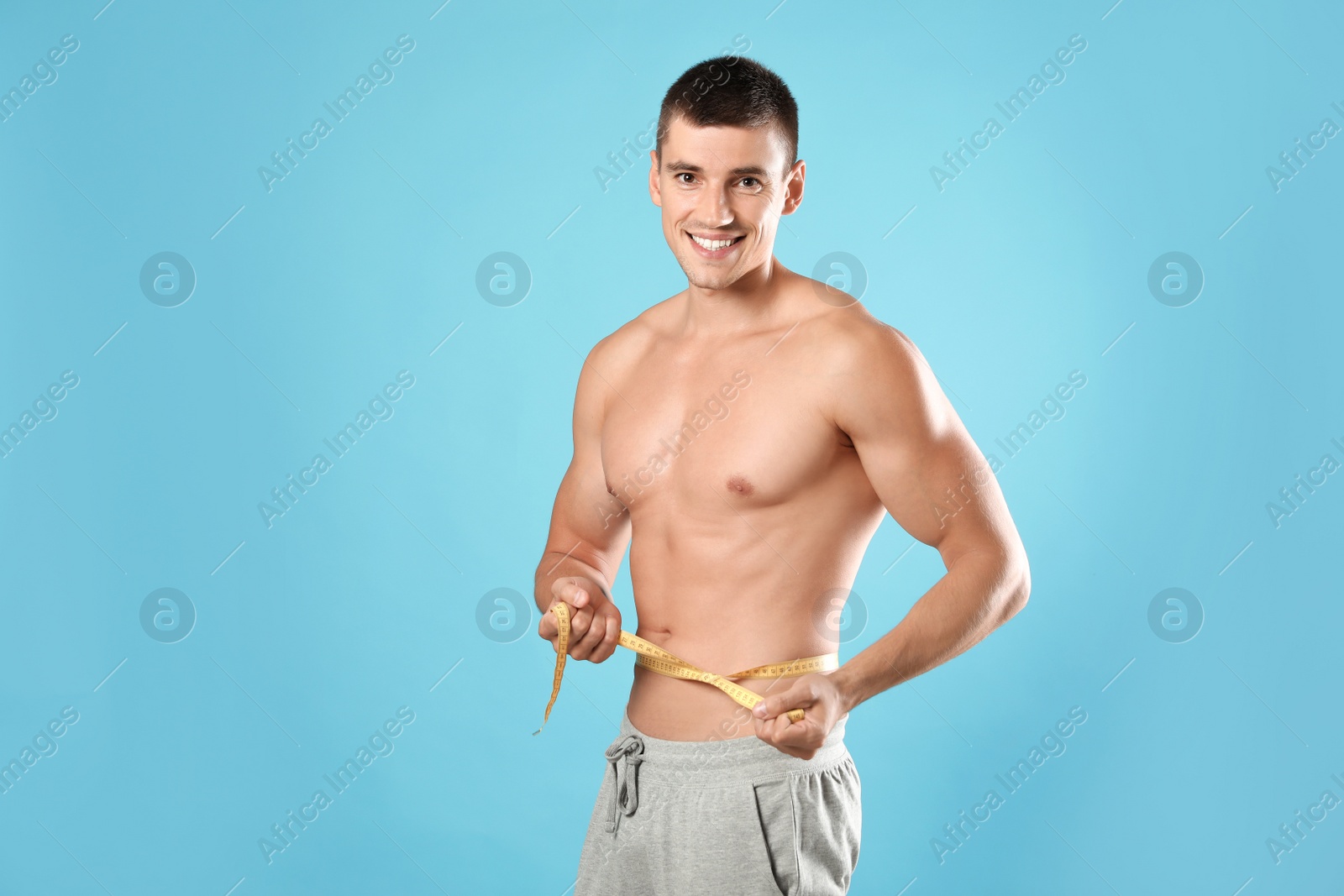 Photo of Young man with slim body using measuring tape on light blue background, space for text