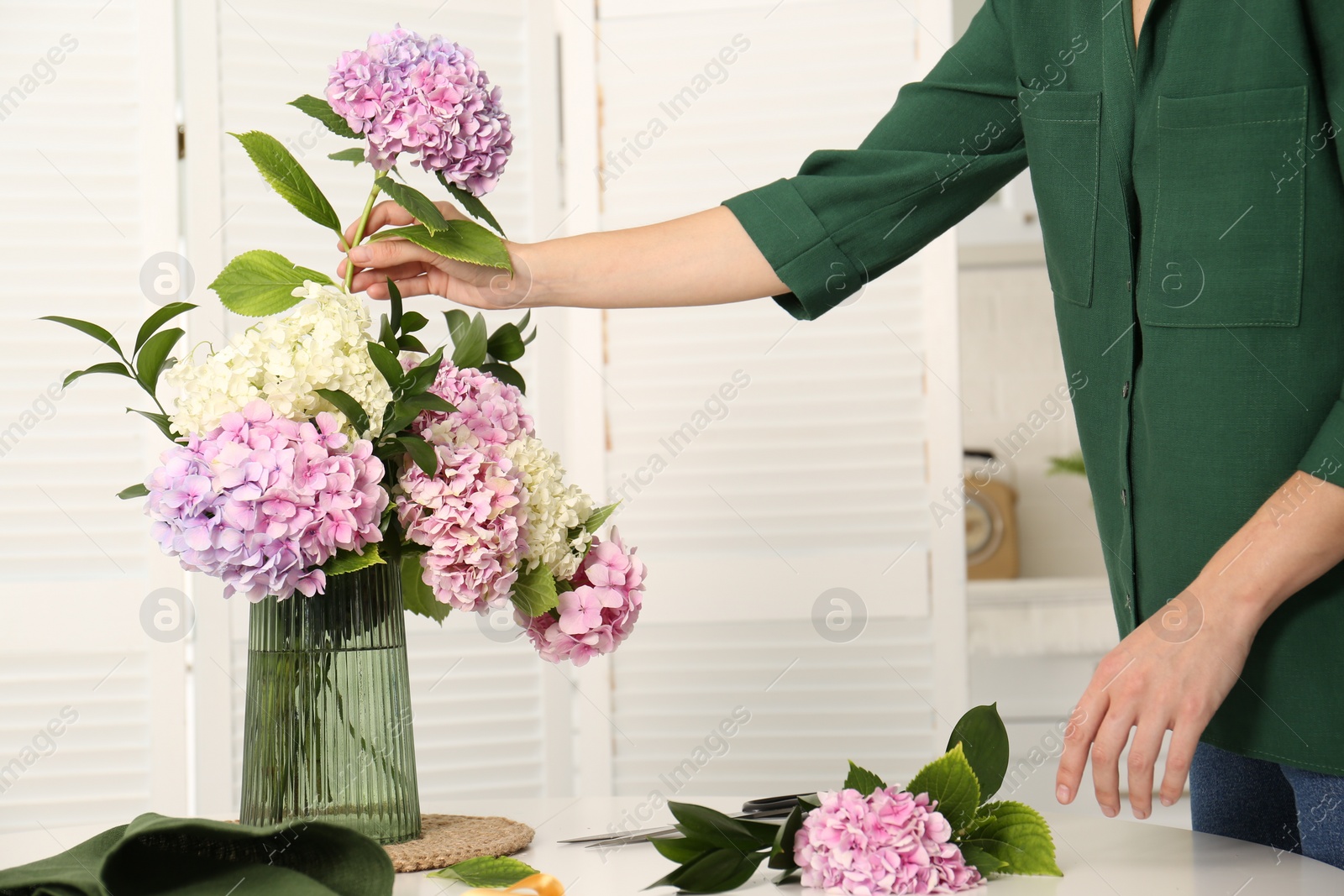 Photo of Woman making bouquet with beautiful hydrangea flowers at table indoors, closeup. Interior design element