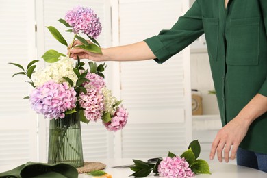 Woman making bouquet with beautiful hydrangea flowers at table indoors, closeup. Interior design element