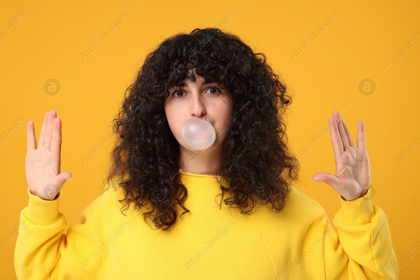 Photo of Beautiful young woman blowing bubble gum on orange background